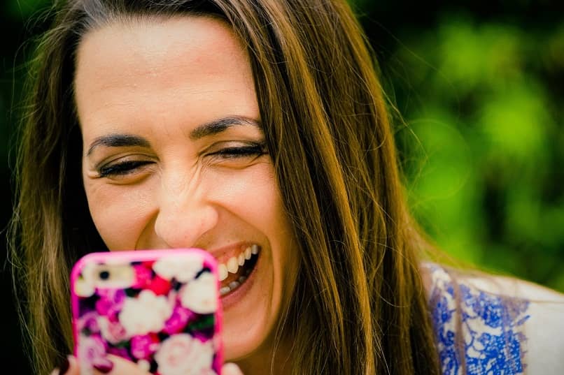 ciemnowłosa kobieta, która patrzy na swój telefon, uśmiecha się radośnie, zmieniając obrazy swoich sieci społecznościowych jako czcionkę w postach na Instagramie