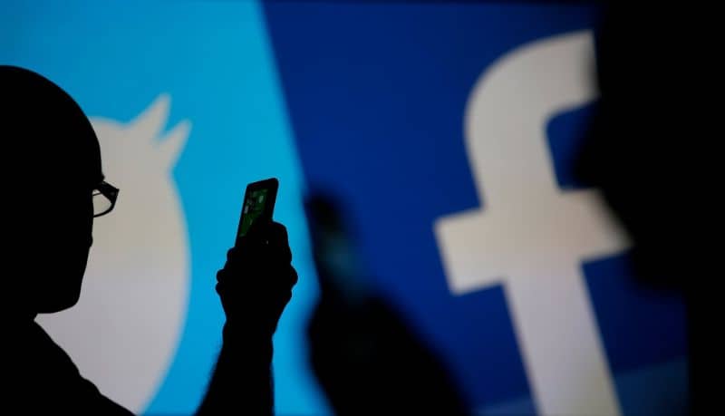 Sylwetka osoby manipulującej telefonem komórkowym z tłem Facebook i Twitter