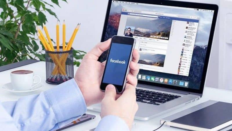 laptop z facebookiem i rękami na telefonie komórkowym z ołówkami facebook i notatnikiem
