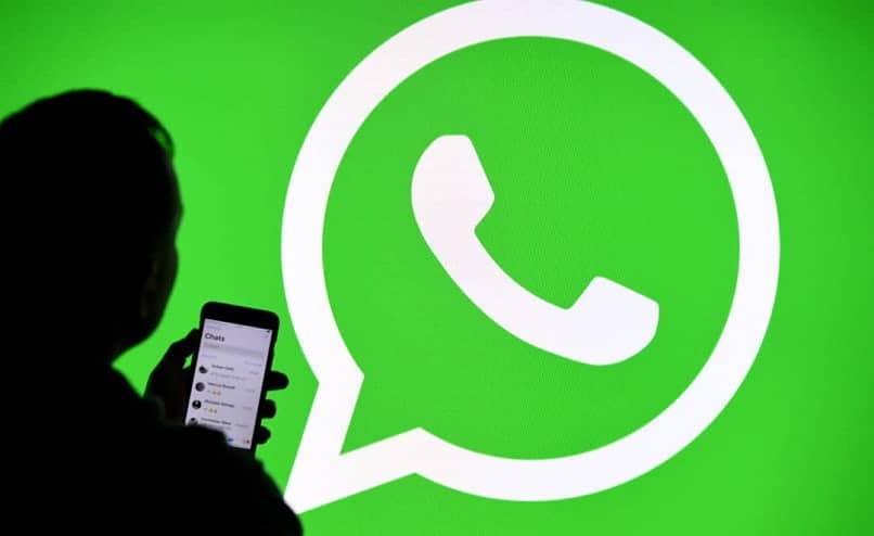 mężczyzna oglądający telefon komórkowy w aplikacji WhatsApp z oficjalnym tłem logo WhatsApp