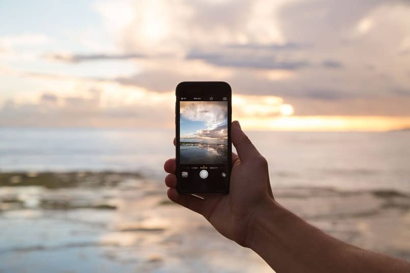 osoba trzymająca telefon komórkowy na plaży